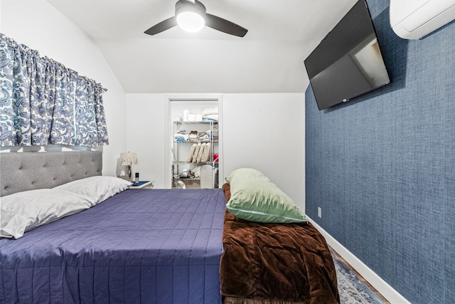 bedroom featuring a spacious closet, wallpapered walls, baseboards, a wall mounted air conditioner, and vaulted ceiling