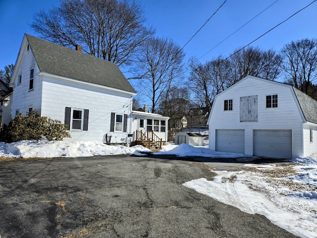 view of snowy exterior featuring an outbuilding, roof with shingles, a chimney, and a gambrel roof