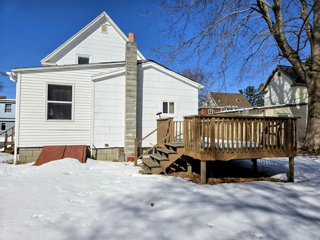 snow covered house featuring a deck and a chimney