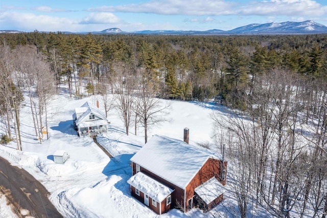 snowy aerial view with a mountain view and a view of trees