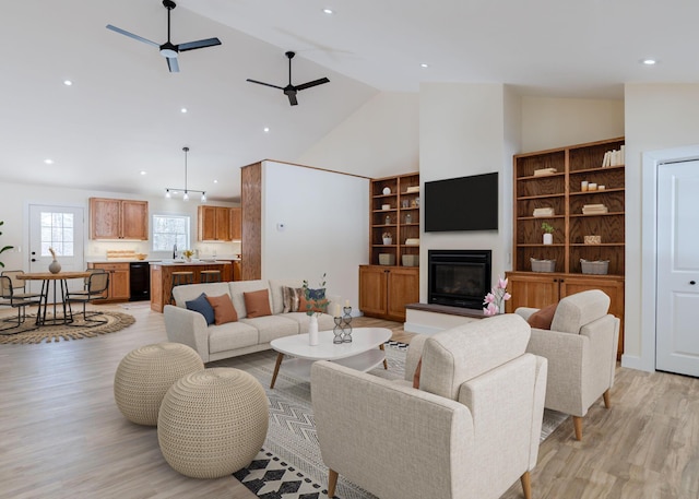 living area featuring recessed lighting, a ceiling fan, a glass covered fireplace, high vaulted ceiling, and light wood-type flooring