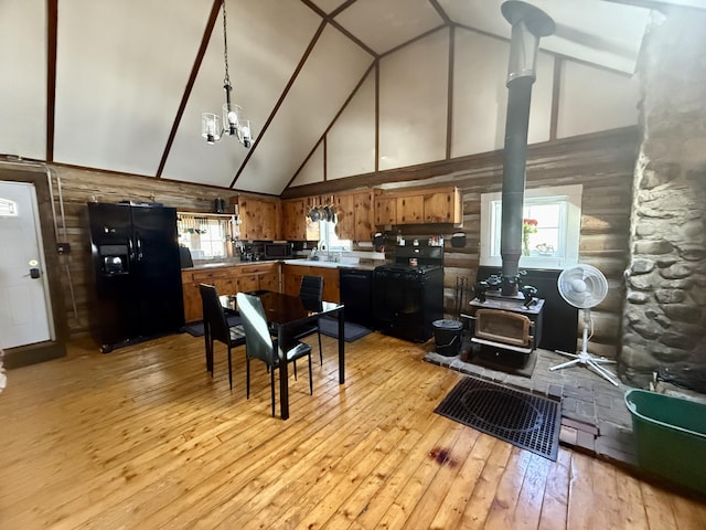 kitchen with light wood-style flooring, a wood stove, black appliances, high vaulted ceiling, and a notable chandelier