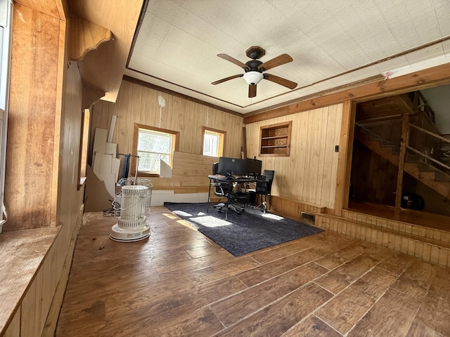 home office with wood walls, wood-type flooring, visible vents, and ceiling fan