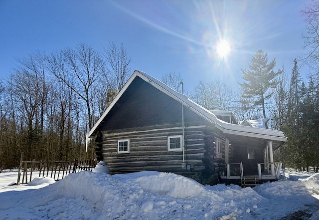 snow covered property with covered porch, a chimney, and log siding