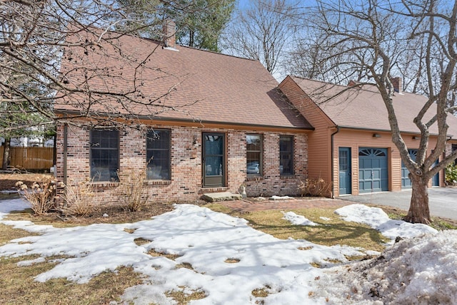 view of front facade featuring driveway, a shingled roof, a chimney, a garage, and brick siding