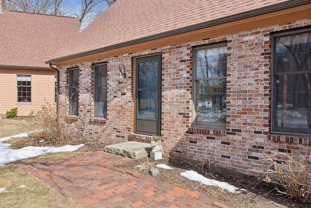 view of exterior entry with brick siding and roof with shingles