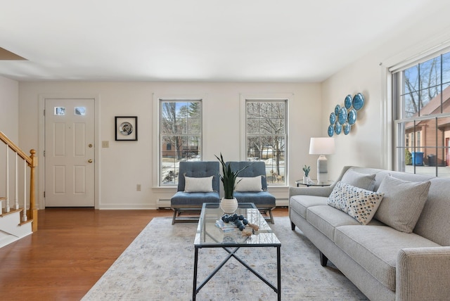 living area featuring a wealth of natural light, stairway, a baseboard heating unit, and wood finished floors