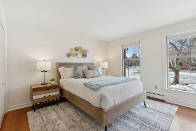 bedroom with multiple windows, baseboard heating, and wood finished floors