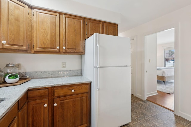 kitchen with light stone counters, brown cabinetry, baseboards, and freestanding refrigerator