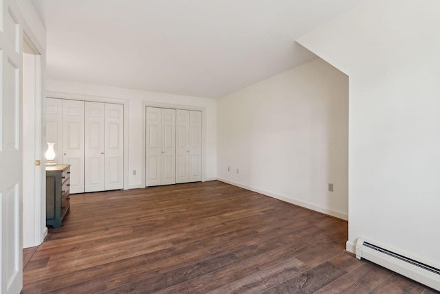 unfurnished bedroom with a baseboard heating unit, dark wood-style floors, multiple closets, and baseboards