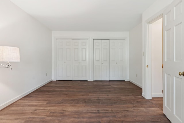 unfurnished bedroom featuring dark wood finished floors, baseboards, and two closets