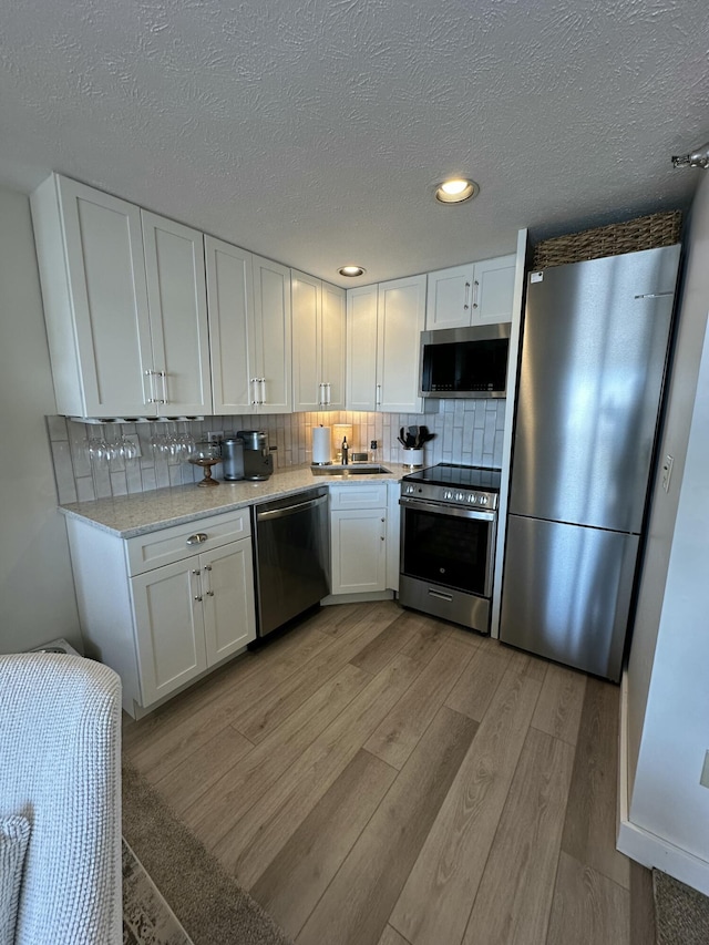 kitchen featuring stainless steel appliances, white cabinetry, backsplash, and light wood finished floors