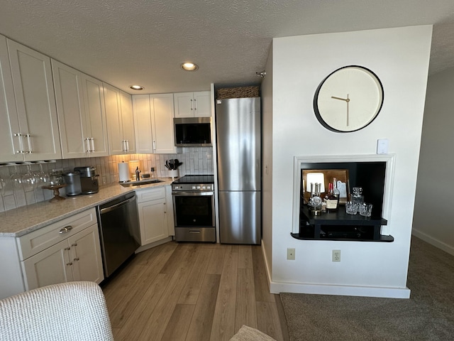 kitchen with appliances with stainless steel finishes, a sink, white cabinetry, and decorative backsplash