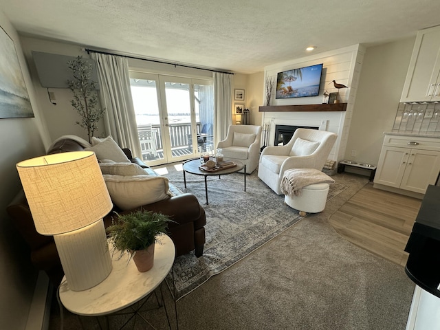 living room with a textured ceiling, recessed lighting, wood finished floors, french doors, and a glass covered fireplace