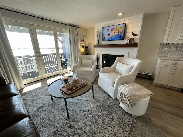 living area with a textured ceiling, french doors, a glass covered fireplace, and wood finished floors