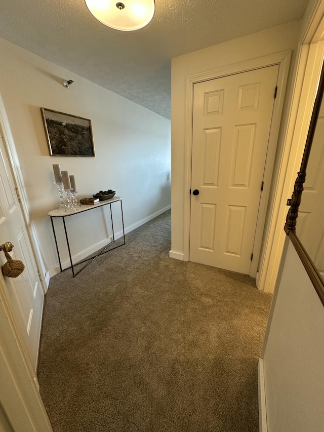 hallway with a textured ceiling, baseboards, and carpet flooring