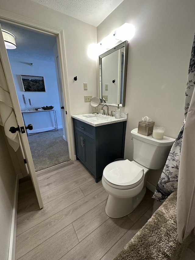 full bath featuring toilet, a textured ceiling, wood finished floors, and vanity