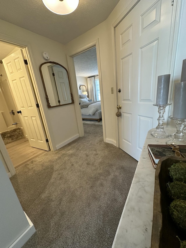 hall featuring carpet floors, a textured ceiling, and baseboards