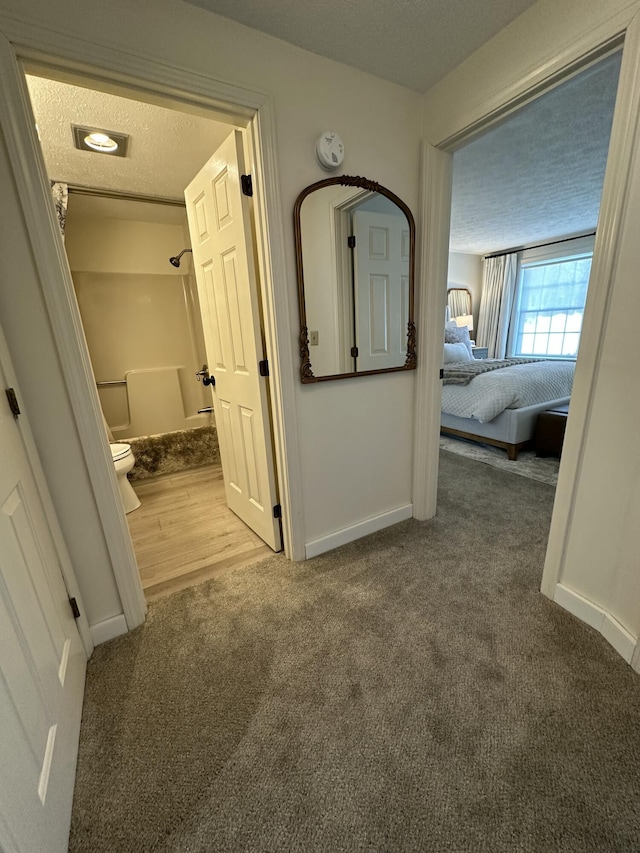 hall featuring carpet flooring, a textured ceiling, and baseboards