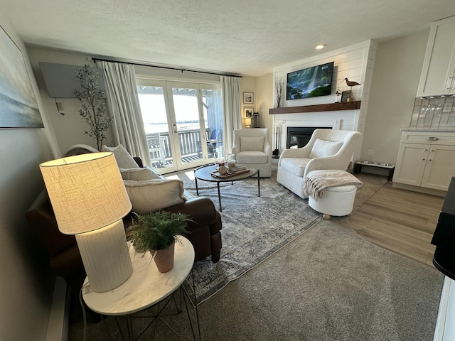 living area with a textured ceiling, french doors, wood finished floors, and a glass covered fireplace