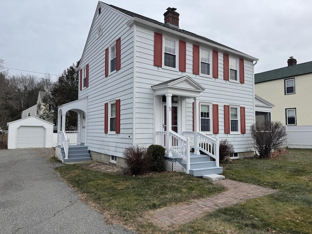 colonial house with a detached garage, a chimney, a front lawn, driveway, and an outdoor structure