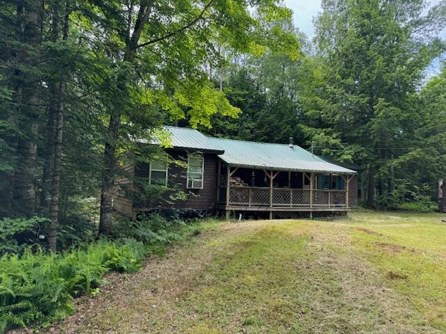 view of front of house featuring a front yard, covered porch, metal roof, and a wooded view