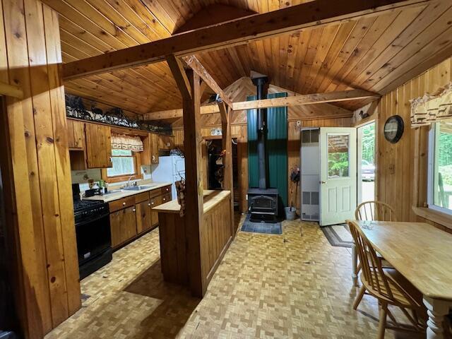 kitchen with lofted ceiling with beams, black gas range oven, a wood stove, wood walls, and a sink