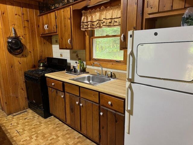 kitchen featuring a sink, light countertops, freestanding refrigerator, decorative backsplash, and gas stove