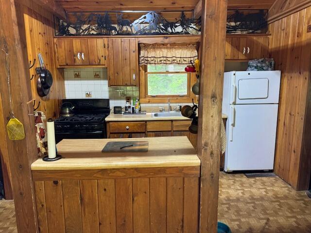 kitchen featuring tasteful backsplash, black range with gas stovetop, brown cabinetry, a sink, and wooden walls