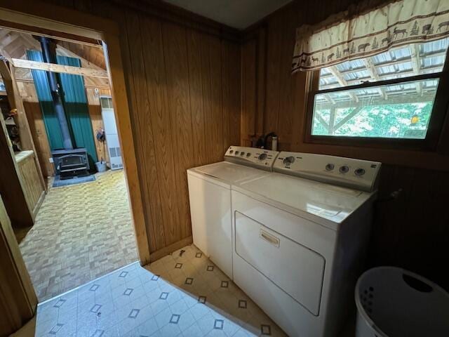 clothes washing area with a wood stove, wood walls, laundry area, and washer and clothes dryer