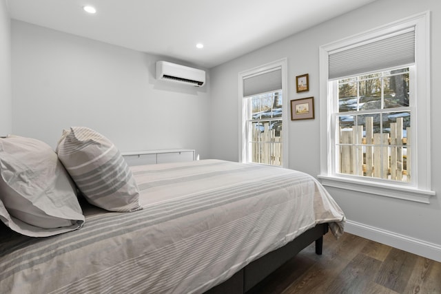 bedroom featuring multiple windows, baseboards, an AC wall unit, and wood finished floors