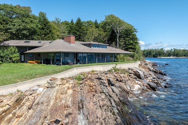 exterior space with a lawn, driveway, a chimney, and a water view