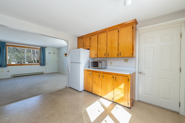 kitchen with brown cabinets, a baseboard radiator, light countertops, stainless steel microwave, and freestanding refrigerator