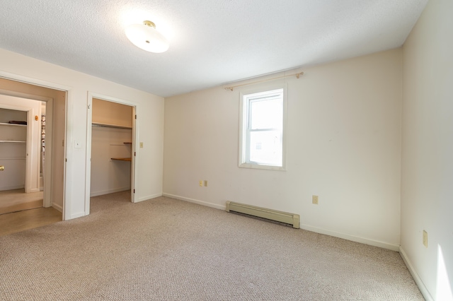 unfurnished bedroom featuring a walk in closet, a baseboard radiator, carpet flooring, a textured ceiling, and baseboards