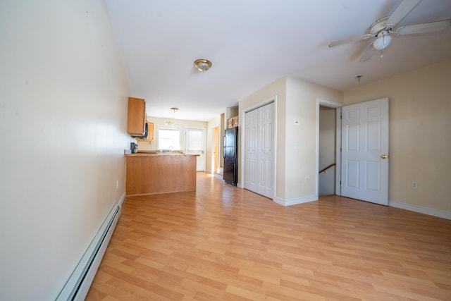 empty room featuring a baseboard heating unit, baseboards, ceiling fan, and light wood finished floors