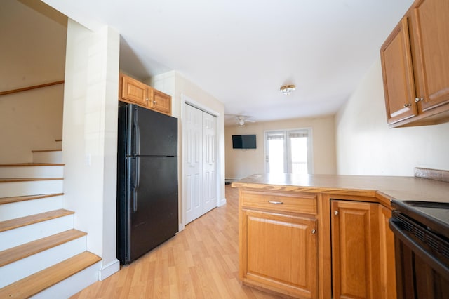 kitchen featuring black appliances, light wood-type flooring, a peninsula, and brown cabinetry