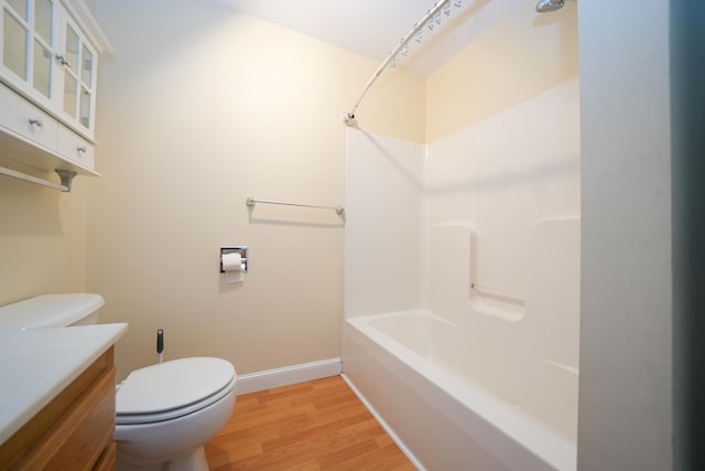 bathroom featuring toilet, wood finished floors, vanity, baseboards, and shower / washtub combination