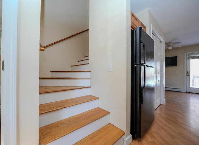 staircase featuring a ceiling fan, a baseboard heating unit, and wood finished floors