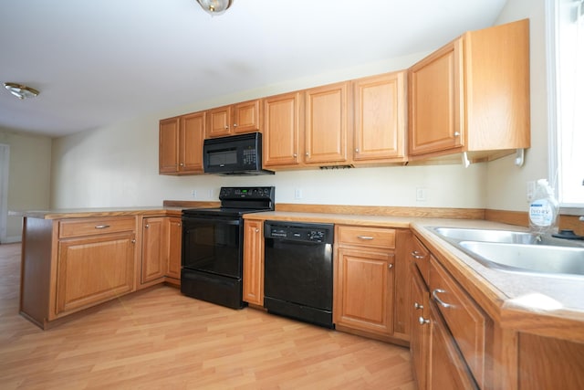 kitchen with light wood-style floors, a peninsula, light countertops, black appliances, and a sink