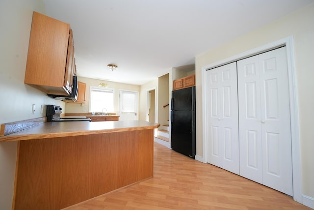 kitchen with light wood-style flooring, a peninsula, a sink, electric stove, and freestanding refrigerator