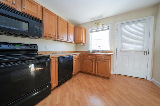 kitchen featuring brown cabinetry, light wood-style flooring, light countertops, black appliances, and a sink