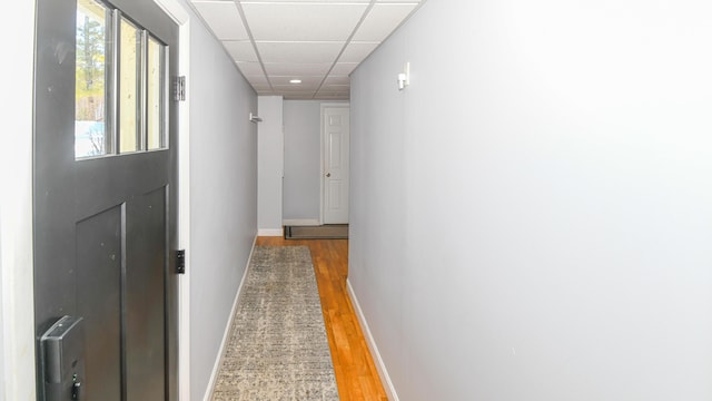 hall featuring light wood finished floors, baseboards, and a drop ceiling