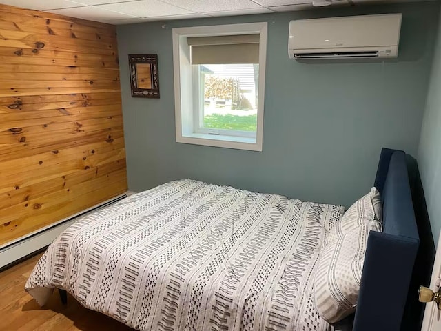 bedroom featuring a paneled ceiling, an AC wall unit, and wood finished floors