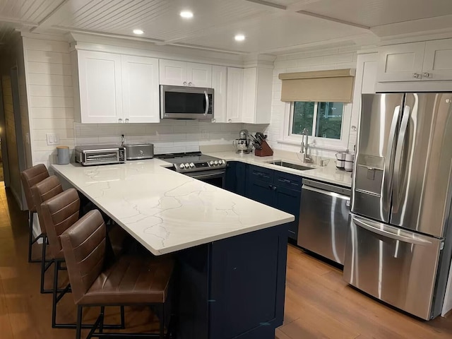 kitchen featuring light wood finished floors, a peninsula, stainless steel appliances, white cabinetry, and a sink