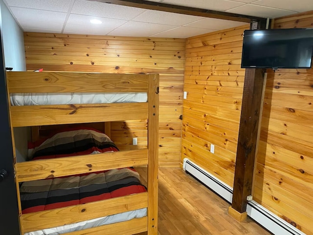 bedroom featuring wooden walls, a baseboard heating unit, a drop ceiling, and wood finished floors