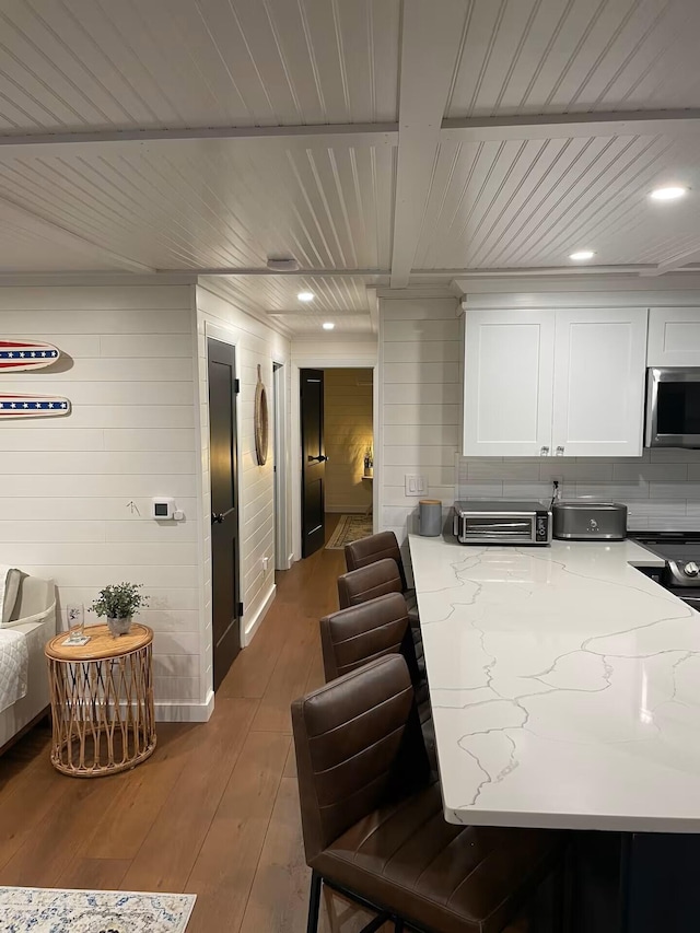 kitchen featuring light stone counters, stainless steel microwave, wood ceiling, white cabinetry, and hardwood / wood-style flooring