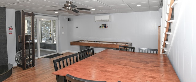 dining room featuring a wall unit AC, a paneled ceiling, ceiling fan, wood finished floors, and baseboards