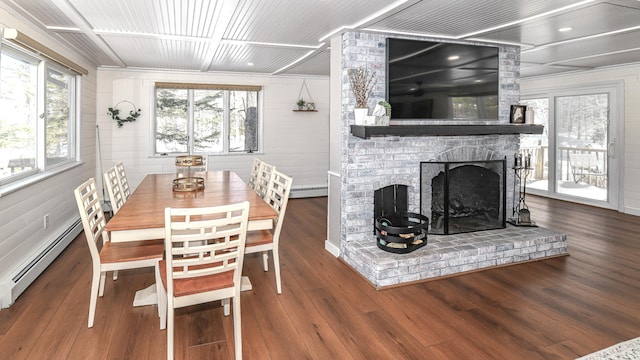 dining area with a baseboard heating unit, a brick fireplace, and wood finished floors