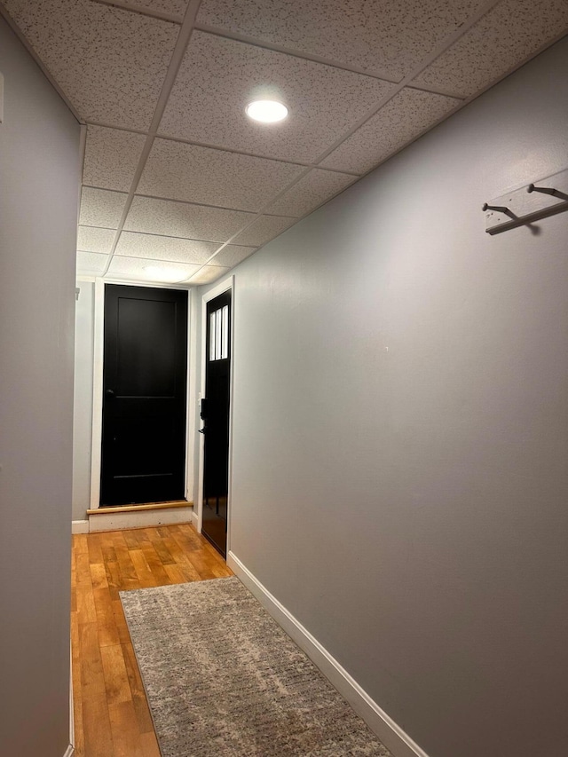 corridor featuring light wood-type flooring, baseboards, and a paneled ceiling