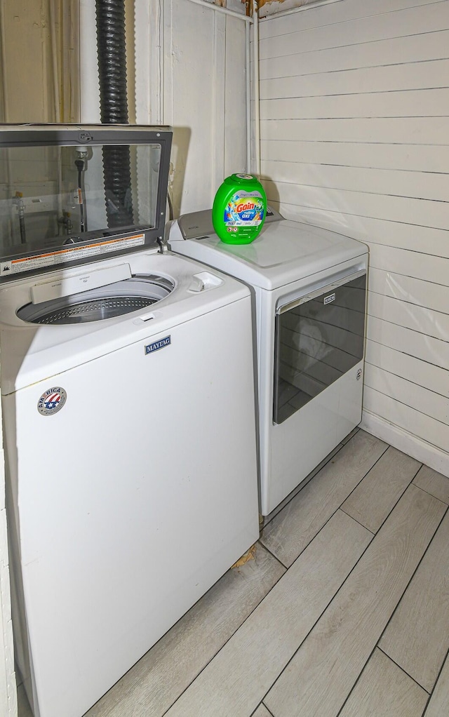 washroom featuring laundry area, wooden walls, light wood finished floors, and separate washer and dryer